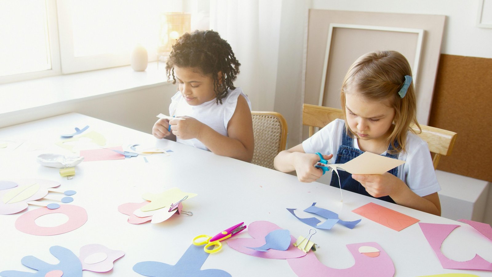 Two children enjoying a creative arts and crafts session indoors with colorful paper and scissors.